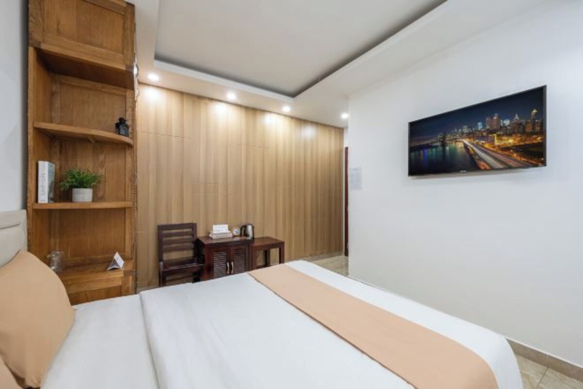 A hotel room with a bed, wooden shelving, a desk, and a cityscape painting on the wall.