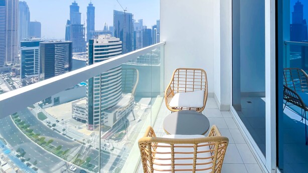 Ein Balkon mit Korbstühlen und einem Tisch, mit Blick auf eine Stadtlandschaft mit modernen Gebäuden.