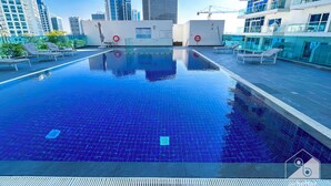 Ein Dachpool mit klarem, blauen Wasser, umgeben von Liegestühlen und Blick auf die Stadt.