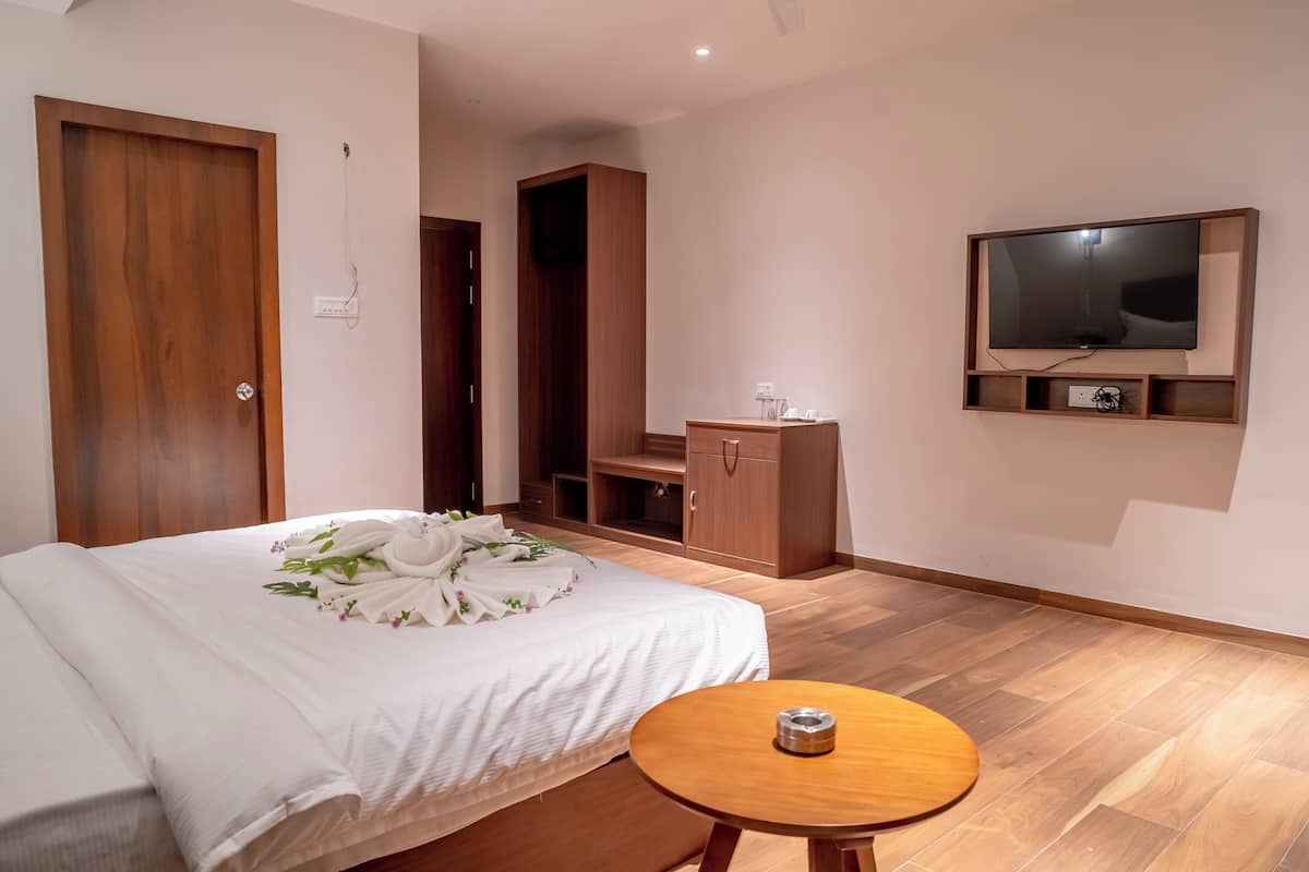 Une chambre d’hôtel moderne avec un lit bien fait, une table de chevet en bois, un téléviseur fixé au mur et une armoire en bois.