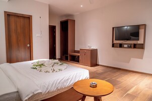 Una habitación de hotel moderna con una cama bien hecha, una mesita de noche de madera, un televisor montado en la pared y un armario de madera.