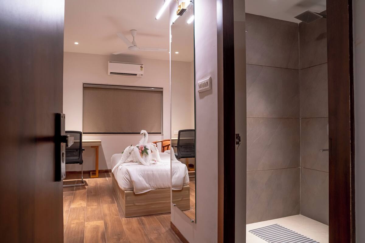 Une chambre d’hôtel moderne avec un grand lit, une douche et un miroir qui reflète la pièce.