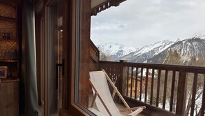 Terraza de madera con una sola silla de descanso con vistas a una cadena montañosa nevada.