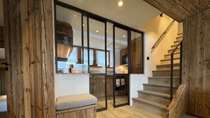 Un interior moderno con un banco de madera, una escalera y una zona de cocina visible a través de puertas de vidrio.