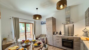 A modern kitchen with a dining area, featuring a large table set with food and drinks, a built-in oven, and a stainless steel range hood.