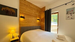 A bedroom with a wooden wall, a bed with white bedding, a nightstand with a lamp, and a window with curtains.