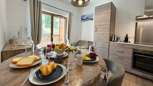 A modern kitchen with a dining table set for two, featuring a variety of fruits and bread.