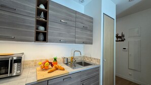 A modern kitchen with grey cabinetry, a stainless steel microwave, and a wooden cutting board with fruits and bread.