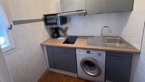 A compact kitchenette with a microwave, coffee maker, sink, and washing machine.