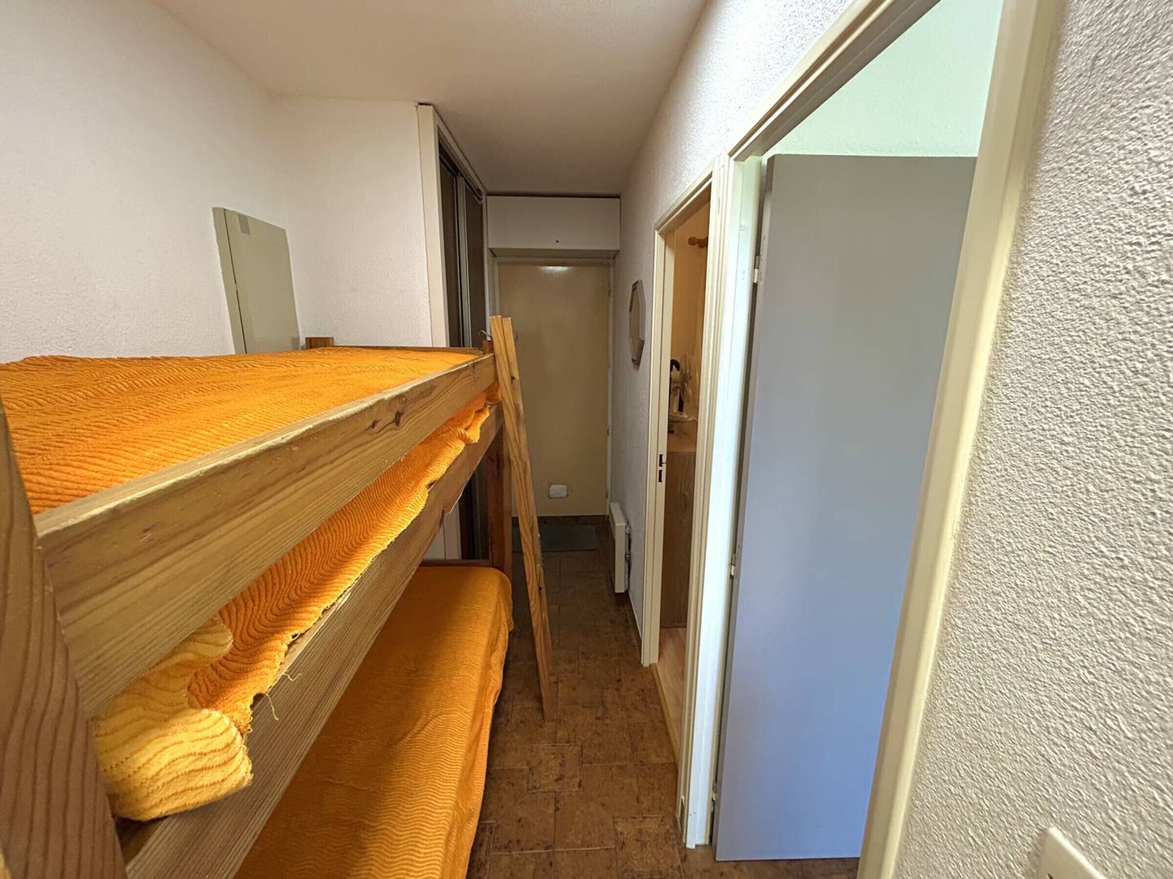 Een smalle gang met een stapelbed en een deur naar een badkamer.