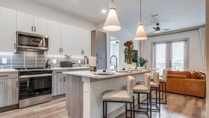 Una cocina moderna con una isla central, electrodomésticos de acero inoxidable e iluminación colgante.