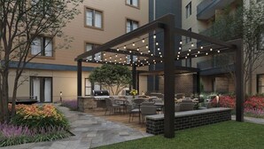 Un patio al aire libre con pérgola, asientos, una parrilla y una jardinera de ladrillo con flores.