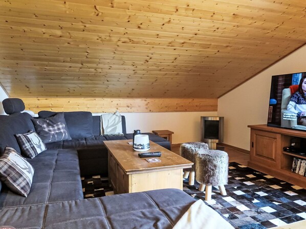 A cozy living room with a wooden ceiling, a dark sofa with patterned cushions, a wooden coffee table, and a television on a stand. - Cosy apartment for 6 guests with WIFI, TV, balcony and panoramic view (Les Diablerets)