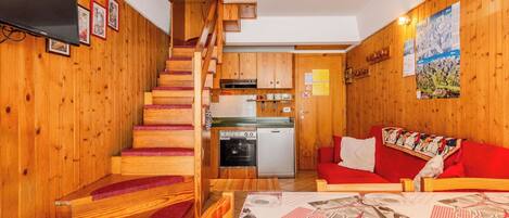 A wooden interior with a staircase, a kitchen, and a red sofa.