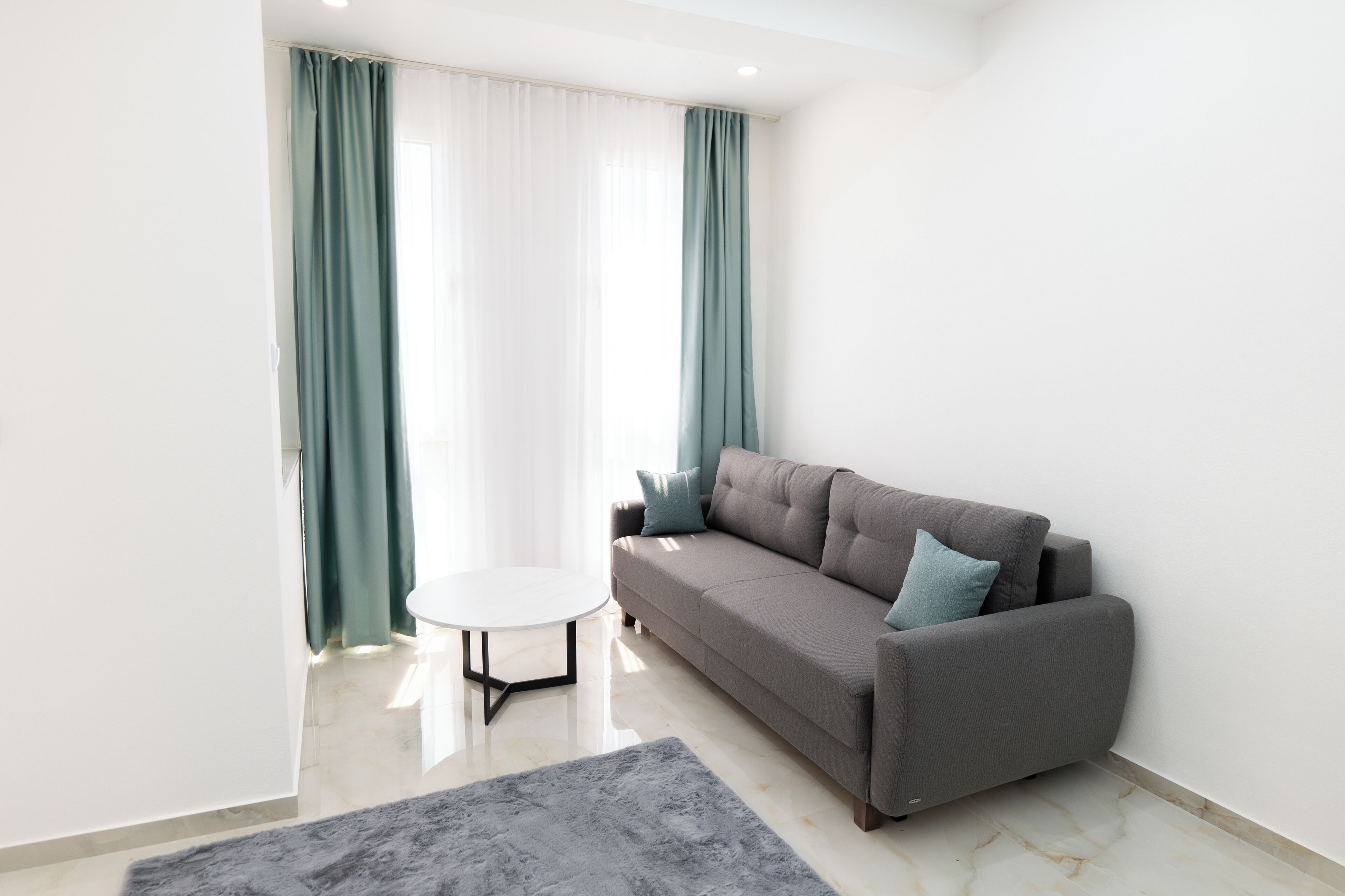 Ein modernes Wohnzimmer mit einem grauen Sofa, einem kleinen runden Tisch und Kordinen in Türkis.