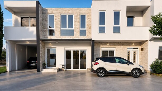 Een modern huis met twee verdiepingen, een oprit, een auto in de garage en een terras.