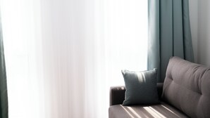 Een hoek van een kamer met een bank en een raam met dunne gordijnen.