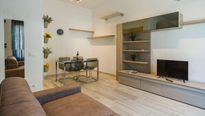 A modern living room with a sofa, a dining table with chairs, a TV, and built-in shelves. - Cosy apartment for 4 people with A/C, WIFI, TV, patio and pets allowed (Camaiore)