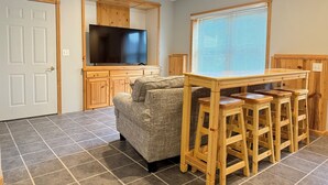 Una sala de estar con un sofá gris, un mueble bajo para televisor de madera y una zona de bar con taburetes.