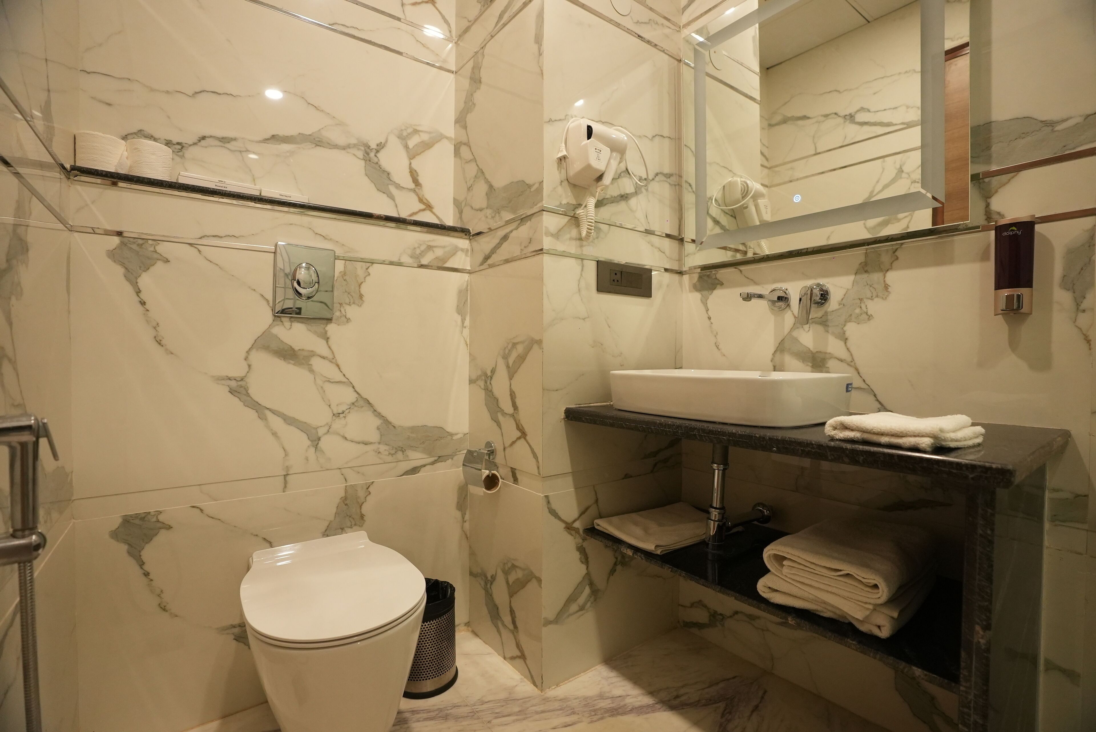 A modern bathroom with a marble wall, a white sink, a towel rack, and a toilet.
