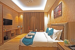 A modern hotel room with a large bed, a desk, a flat-screen TV, and a painting on the wall.