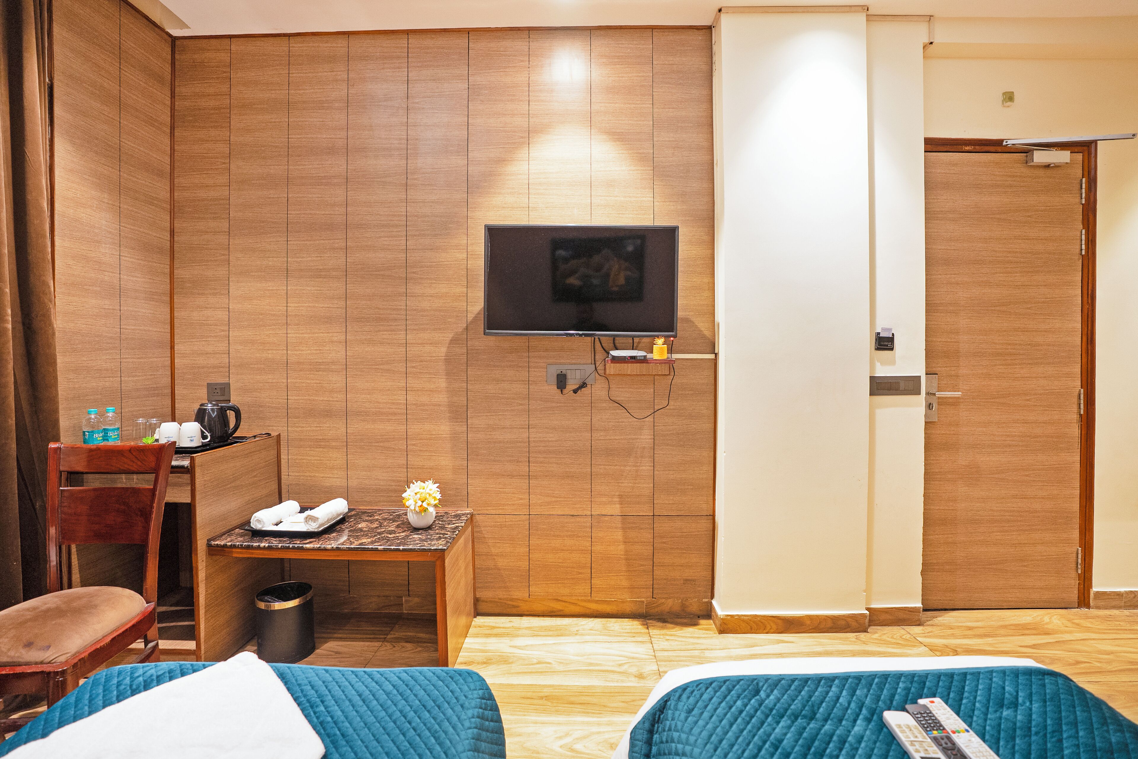 Habitación de hotel con dos camas, un televisor montado en la pared, un escritorio con una silla y un armario de madera.