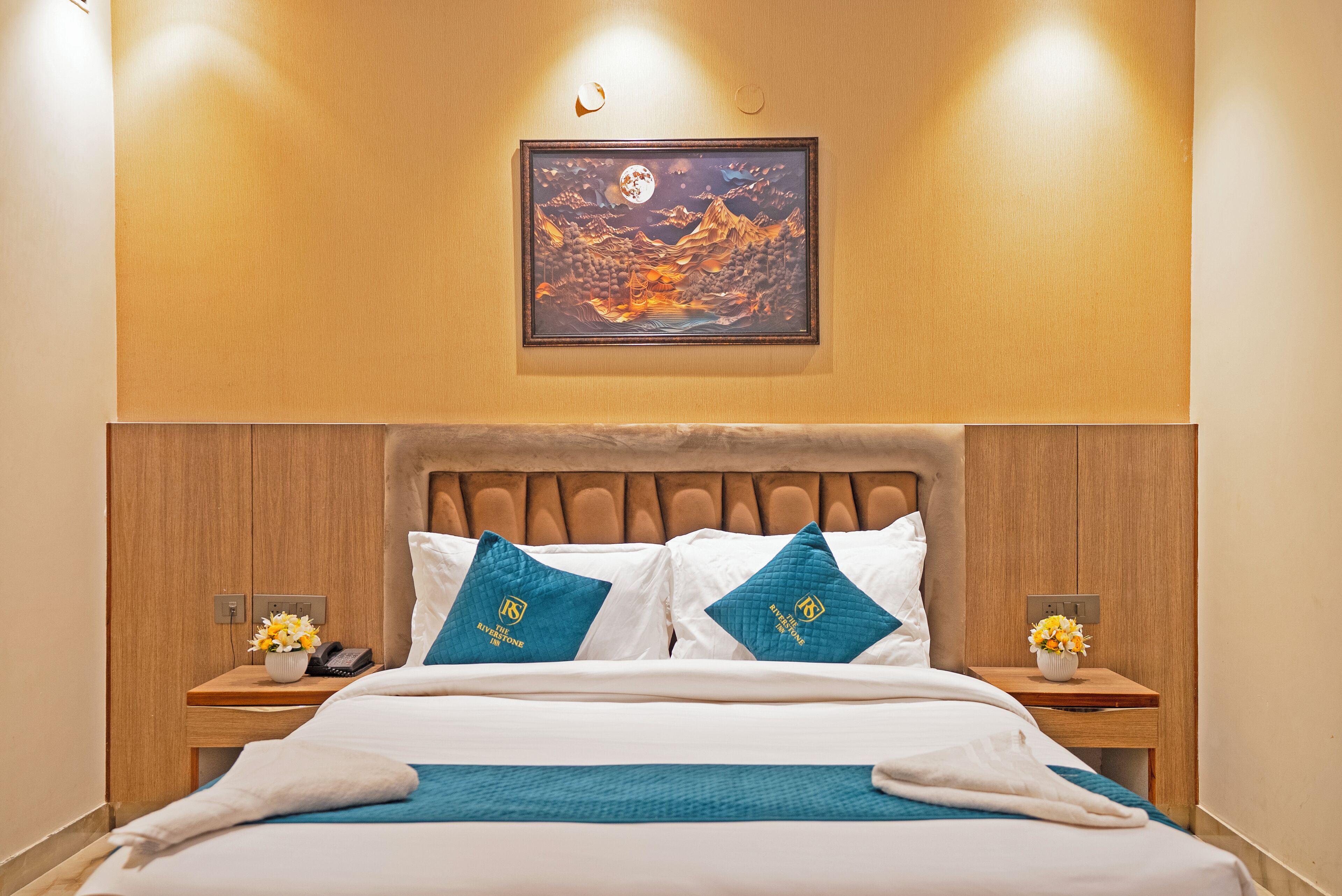 A neatly made bed with white and blue bedding, two bedside tables with lamps, and a framed artwork above the bed.