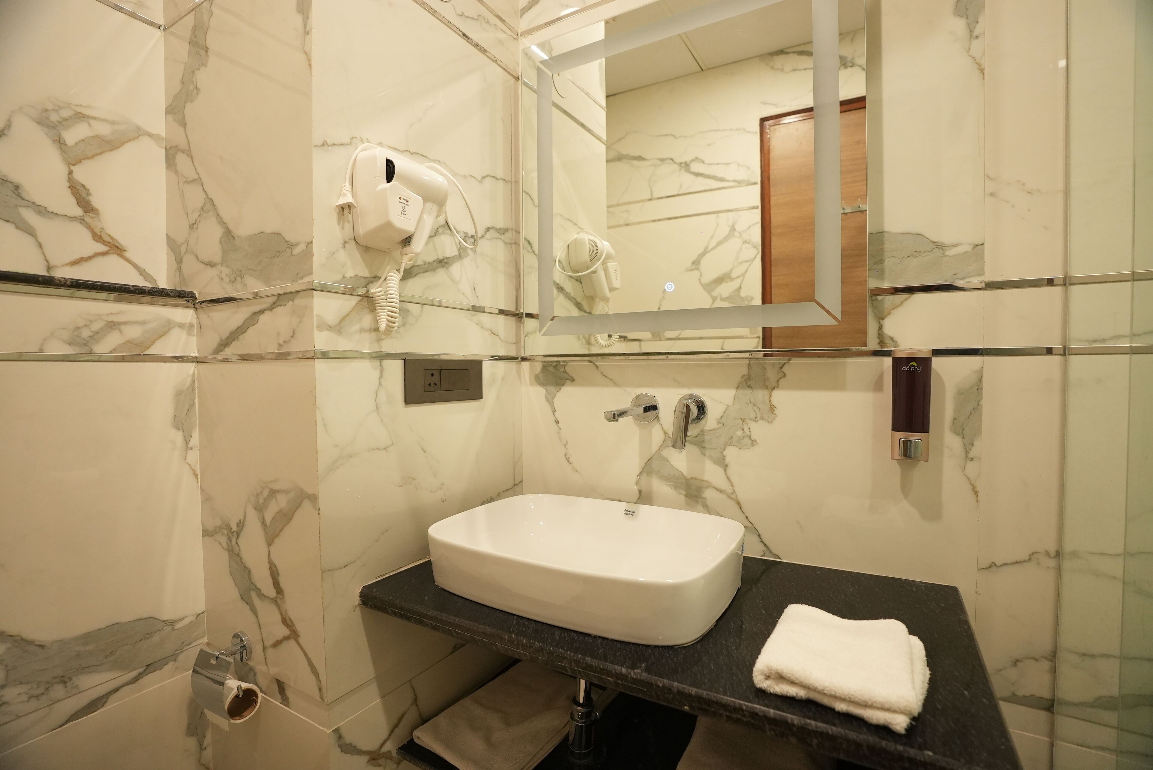 A bathroom with a marble wall, a white sink, a black countertop, a towel, and a hairdryer mounted on the wall.