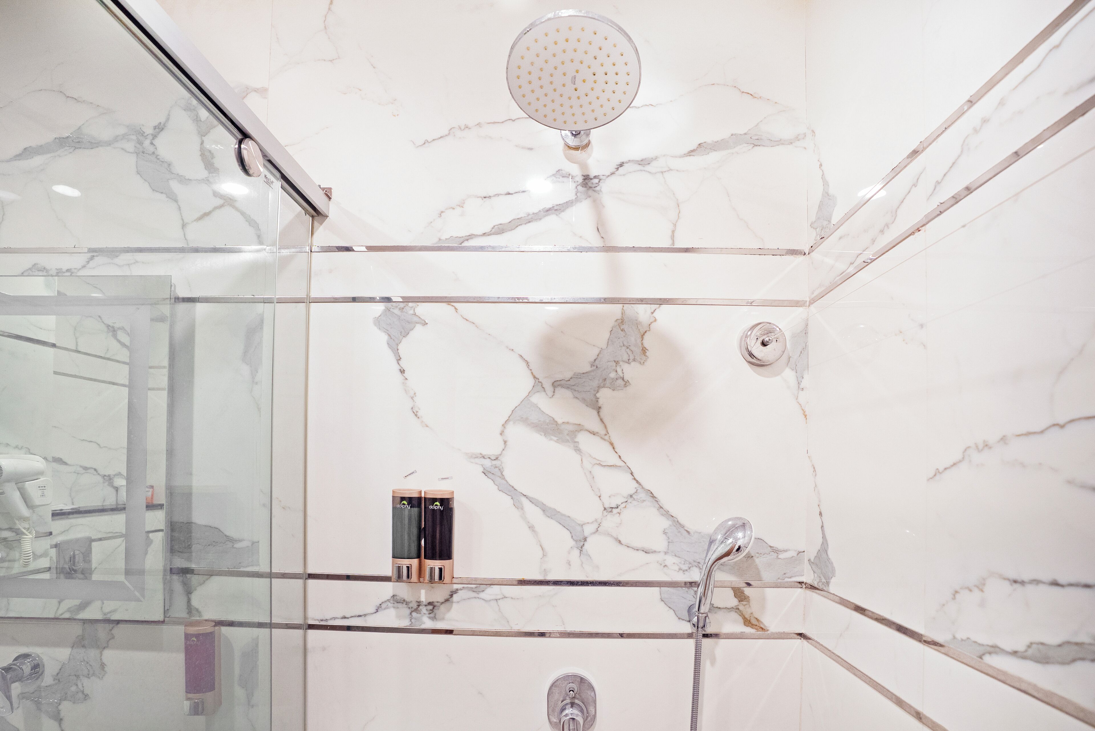 A modern bathroom with a glass-enclosed shower, marble walls, and a visible hairdryer.