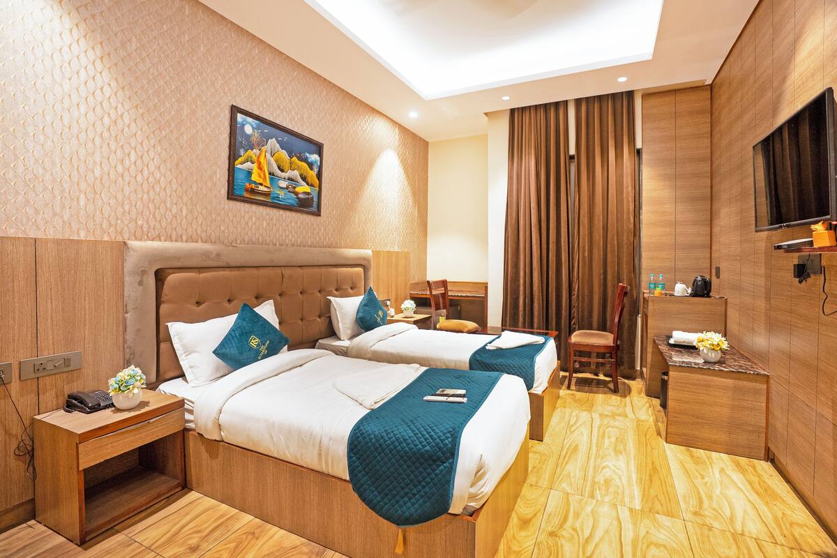 Habitación de hotel con dos camas, un escritorio, una silla, un televisor y un cuadro en la pared.