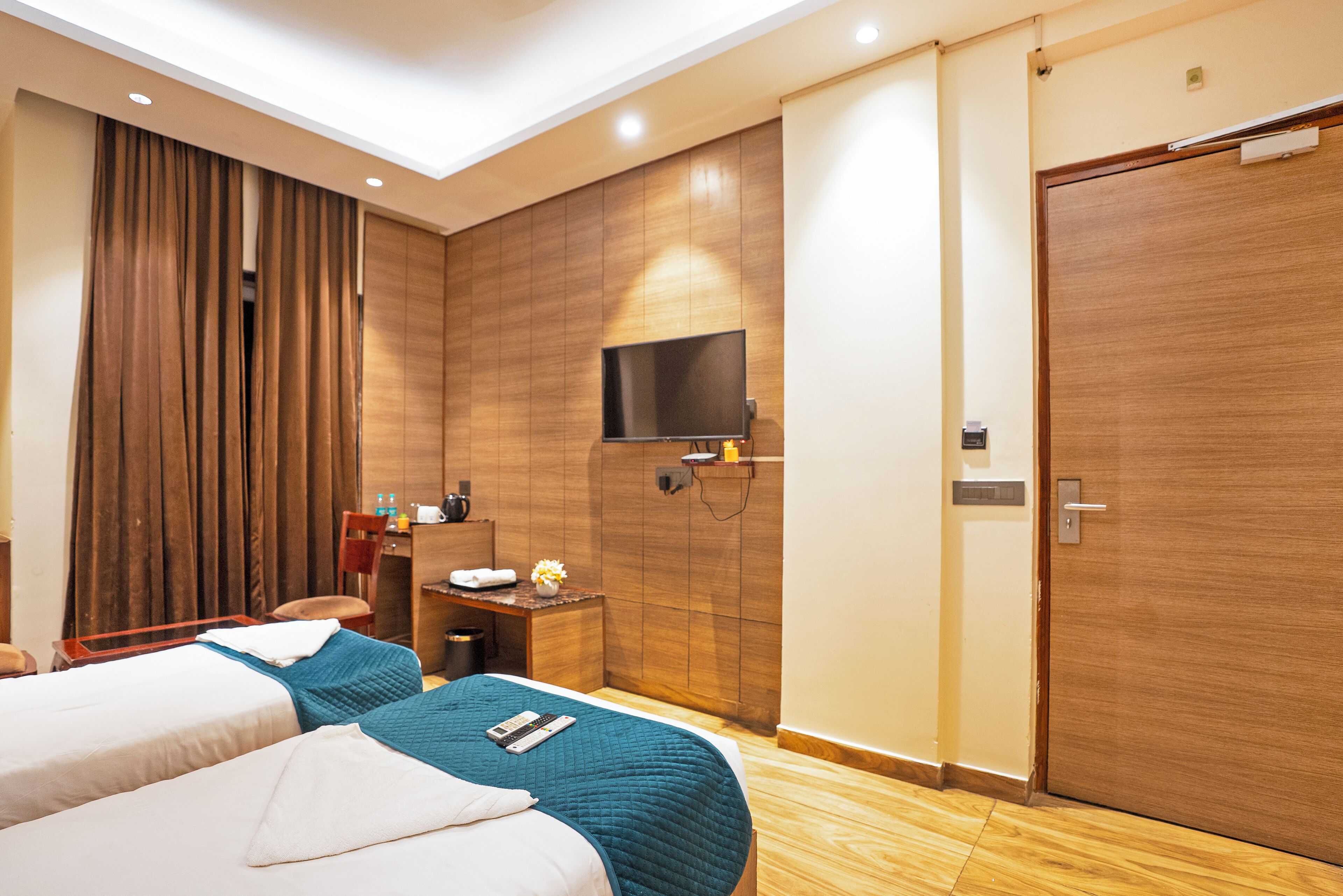 A hotel room with two beds, a desk with a chair, a television, and a wardrobe.