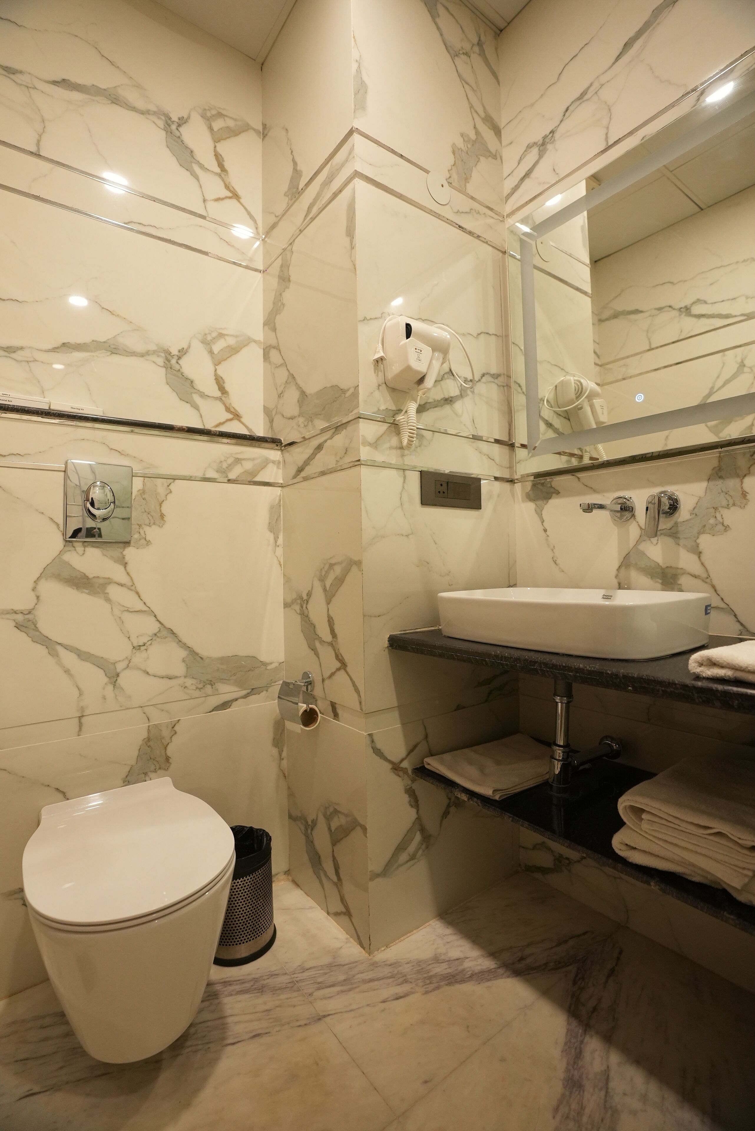A bathroom with a marble wall, a white sink, a mirror, a towel rack, and a toilet.