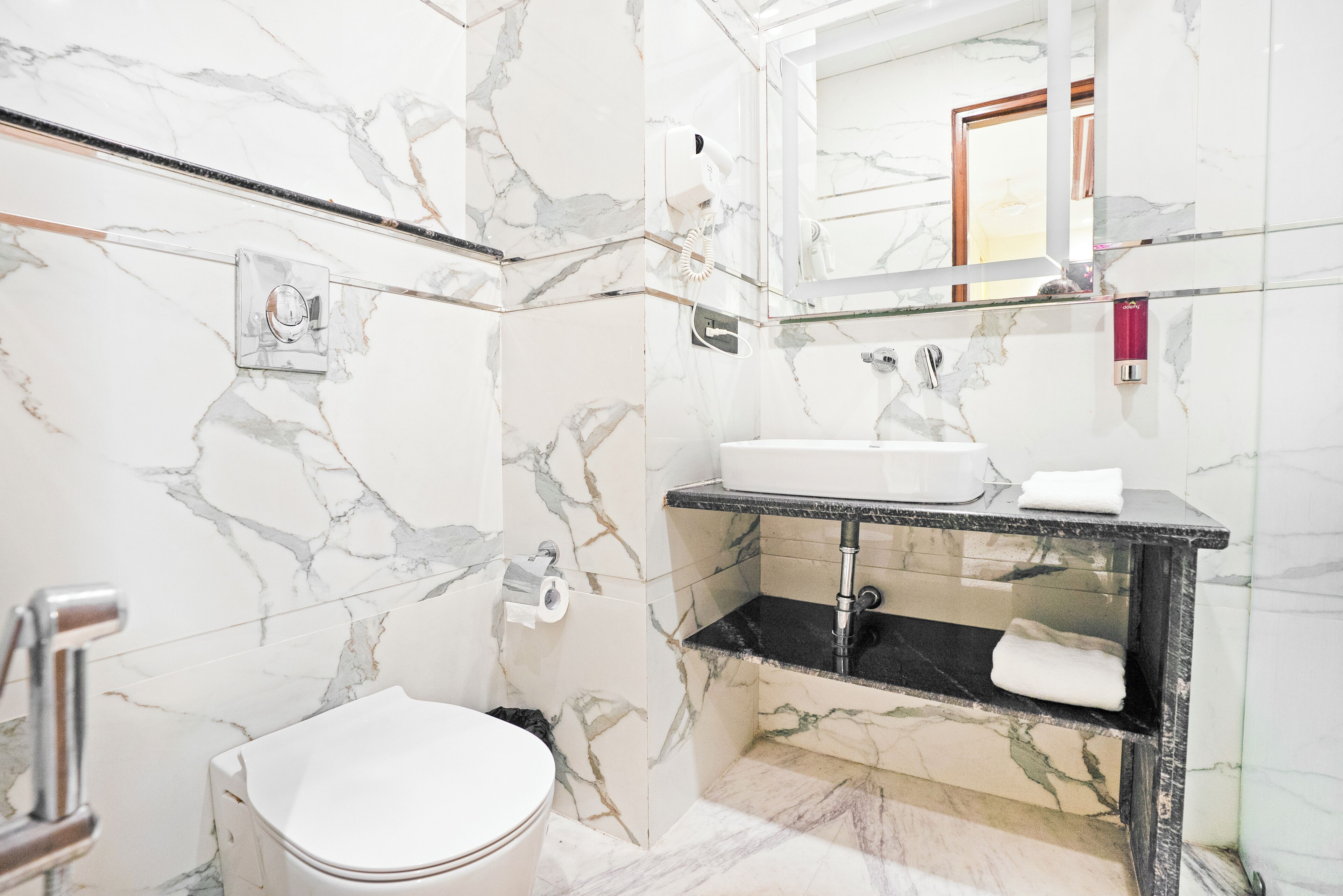 A bathroom with a marble floor, a white toilet, a sink with a black countertop, and a mirror above the sink.