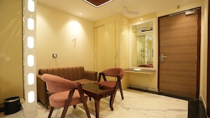 A modern room with a sofa, two chairs, a glass table, a wooden door, and a mirror. - The Riverstone Inn - Near India Expo Centre & Mart, Greater Noida (Greater Noida)