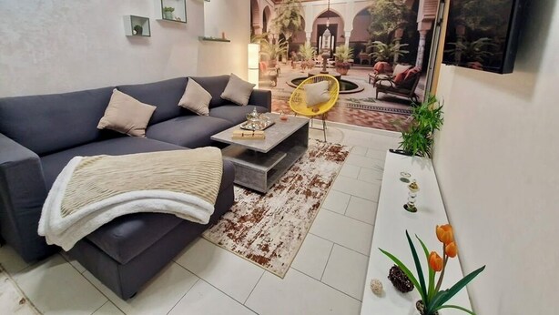 Ein Wohnzimmer mit einem dunklen Sofa, einem gelben Sessel und einem Couchtisch. An der Wand hängt ein großes Gemälde eines Innenhofs.