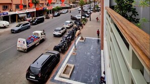 Blick von einem Balkon auf ein belebtes Stadtgebiet mit mehreren Gebäuden, parkenden Autos und einem Café.