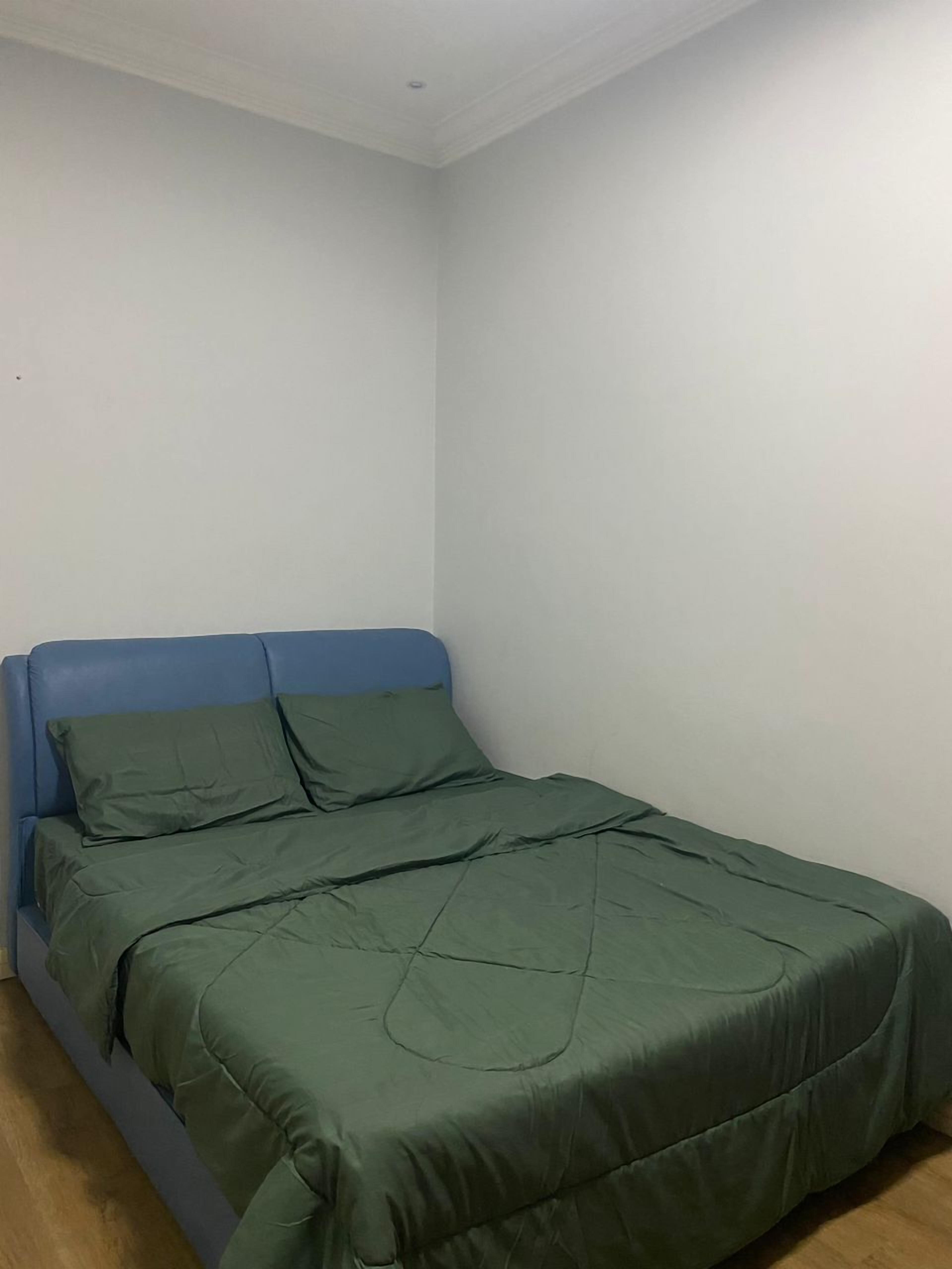 Una habitación pequeña con cama individual, cabecera azul y ropa de cama verde.