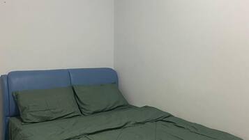 Una habitación pequeña con cama individual, cabecera azul y ropa de cama verde.