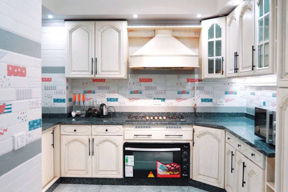 Una cocina con armarios blancos, estufa y microondas.