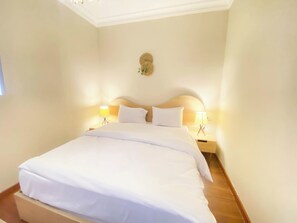 A neatly made bed in a hotel room with a wooden headboard, two bedside lamps, and a small decorative item on the wall.
