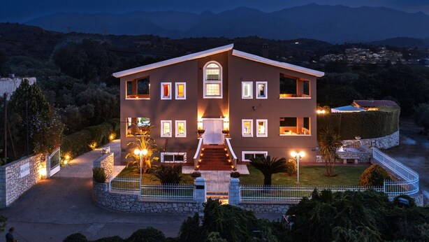 A two-story building with a central entrance, multiple windows, and a well-lit facade. - Villa Clio, with Mountain view (kalyves Armenoi)