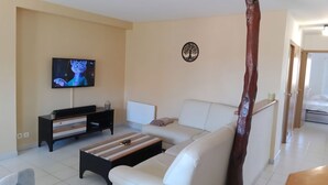 Un saló amb un sofà blanc, una taula baixa de fusta, una televisió penjada a la paret i una obra d'art mural amb forma d'arbre decoratiu.