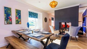 Uma sala de jantar com mesa de madeira posta para quatro pessoas, bancos e um lustre moderno.