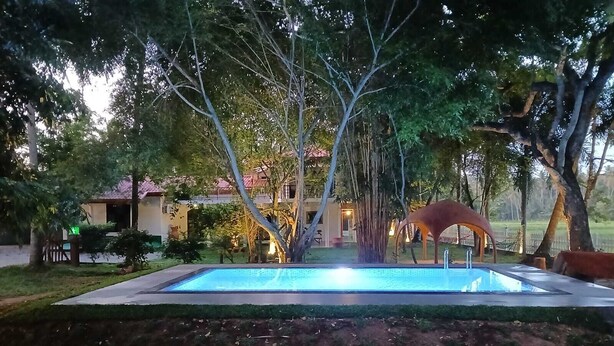 A rectangular pool with a fountain in the center, surrounded by trees and a building with a red roof in the background. - 4-bedroom villa in wonderful Kadahapola with WiFi, AC, fitness room (Kadahapola ,Narammala)