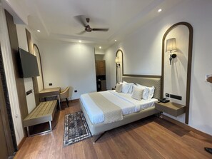 Una habitación de hotel moderna con una cama grande, un escritorio, una silla, un ventilador de techo y un televisor fijado a la pared.