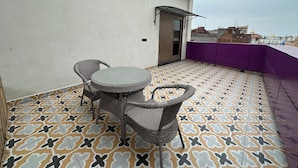 A rooftop terrace with a patterned floor, two wicker chairs, a small table, and a door leading to an indoor area. - Hotel Temple City by Novelty (Amritsar)