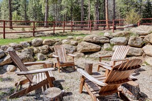 A set of Adirondack chairs in a forested area with a wooden fence and large rocks. - Cozy Mountain Cabin Close to Town (Darby)
