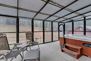 A covered patio area with a hot tub, two chairs, and a view of a forest.