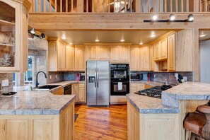 A modern kitchen with wooden cabinets, granite countertops, stainless steel appliances, and a central island.