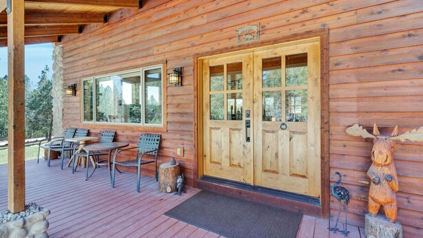 Een houten chalet met veranda, een eethoek met metalen stoelen en een grote houten deur.